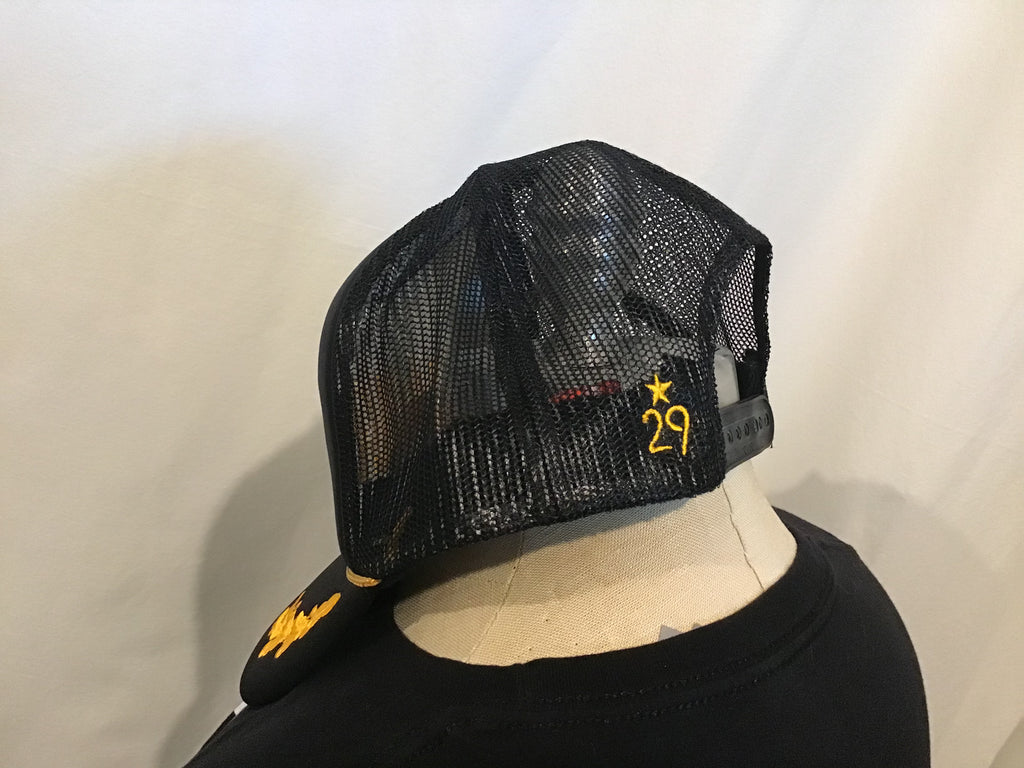 left side of a foam front black trucker the 29th state apparel logo embroidered in gold on back left panel by the plastic snapback