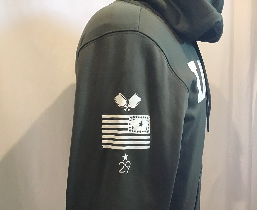 A side view of an army green olive sweatshirt with the hood up on a mannequin focus on the right sleeve with two crossed pickleball paddles the 29 star iowa flag and the 29th state apparel logo all in white screen print