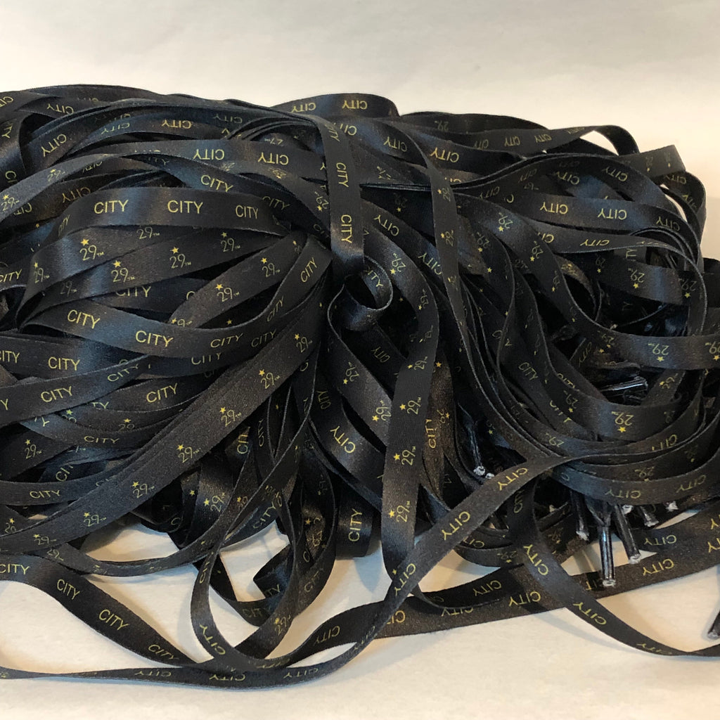 a closeup photo of pile of black silky shoe laces city and the 29th state logo in gold on either sides