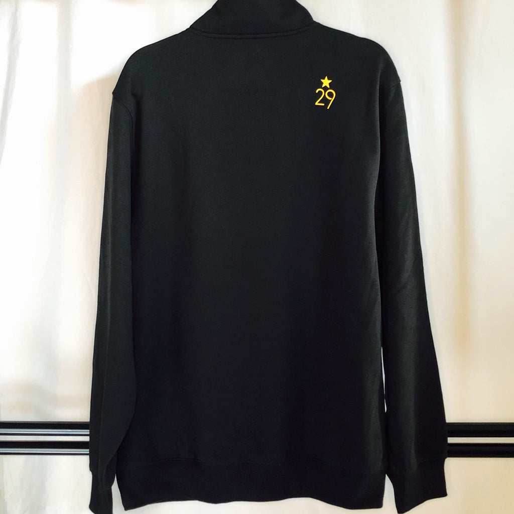 the back of a black 1/4-zip sweatshirt hanging from the hanger with the 29th state apparel logo screen printed on the upper right shoulder in gold