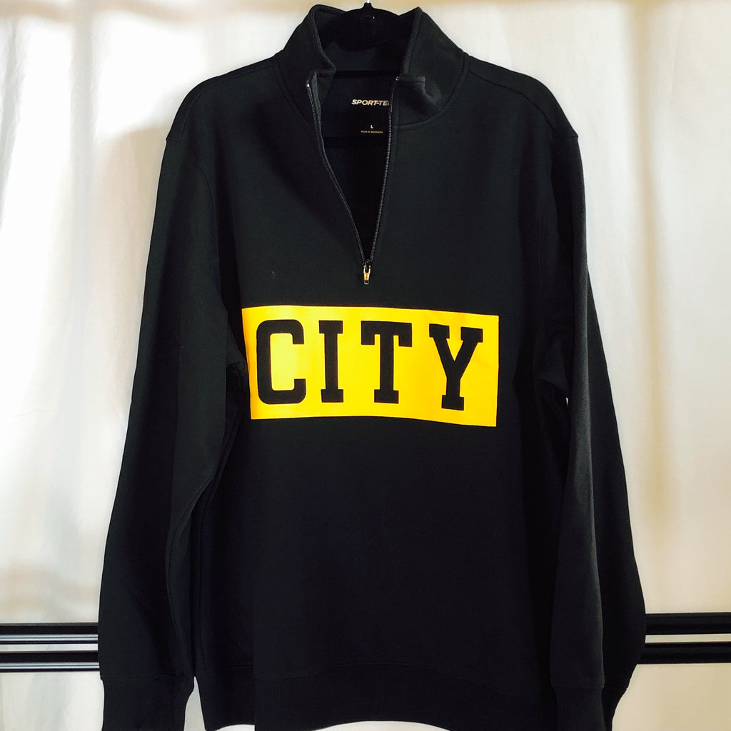 a black 1/4-zip sweatshirt hanging from a hanger with a thick, bold stripe screen-printed across the front and "city" cut out in black