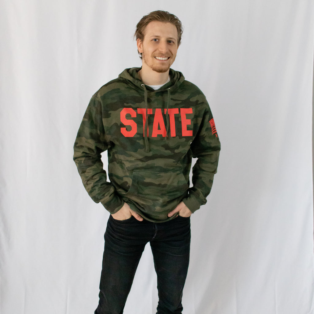 dirty blonde male in a military green camo hoodie state in red printed on front with details printed on left sleeve