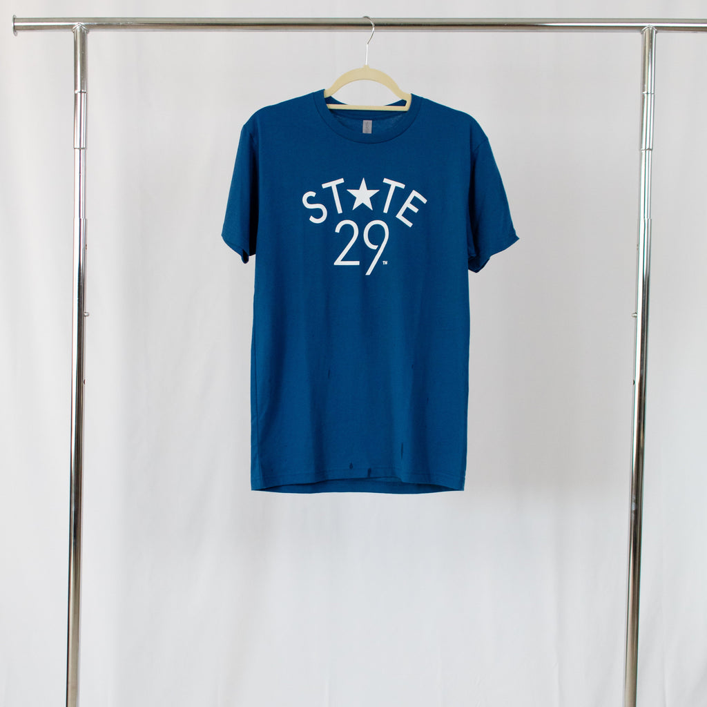 cool blue tee shirt with 29th state apparel logo in white centered on front hanging from silver rack