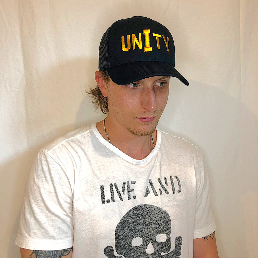 young man gazing to the right wearing an all black trucker hat with unity embroidered on front in gold