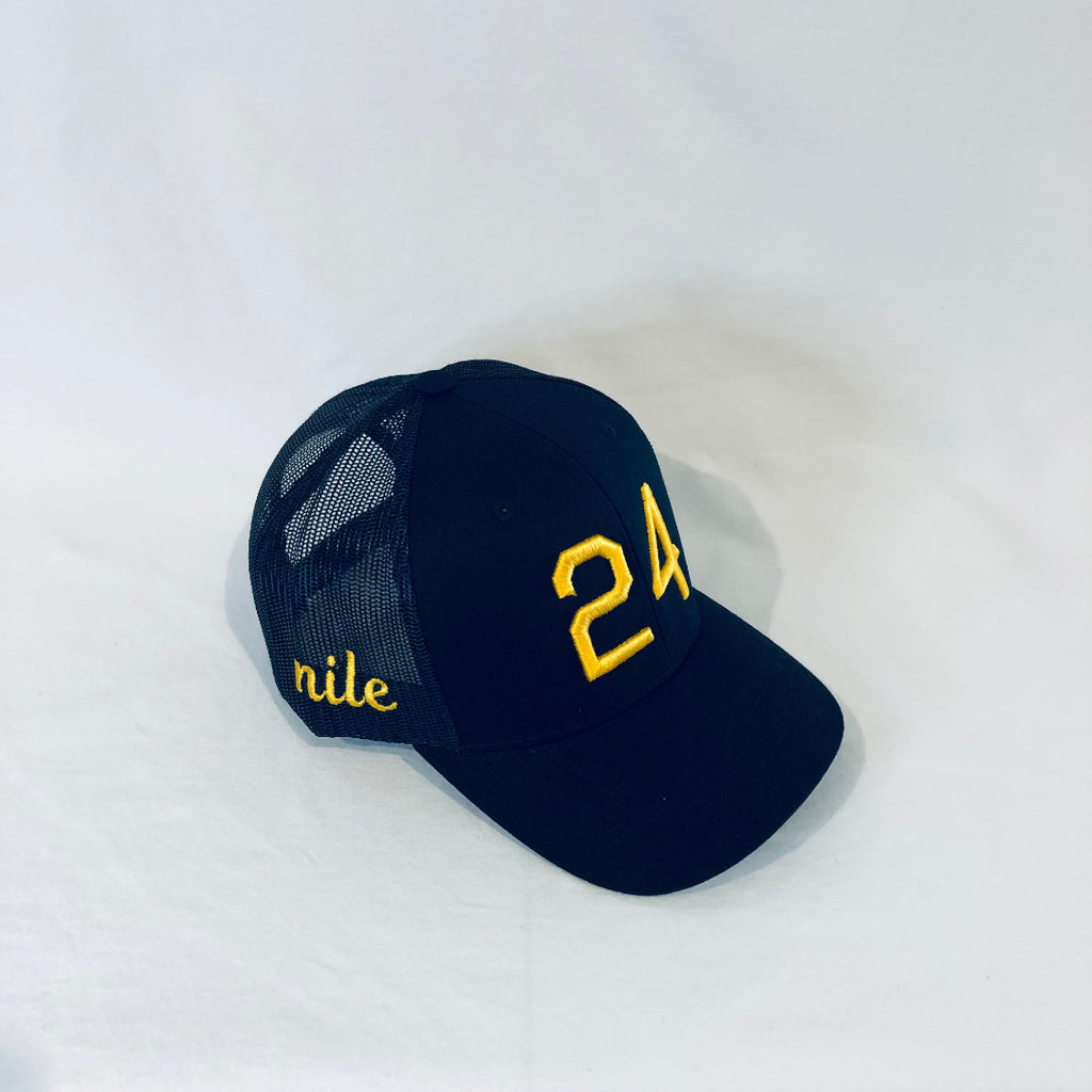 an all black trucker hat with 24 on the front and nile in cursive on the right side all in gold puff embroidery