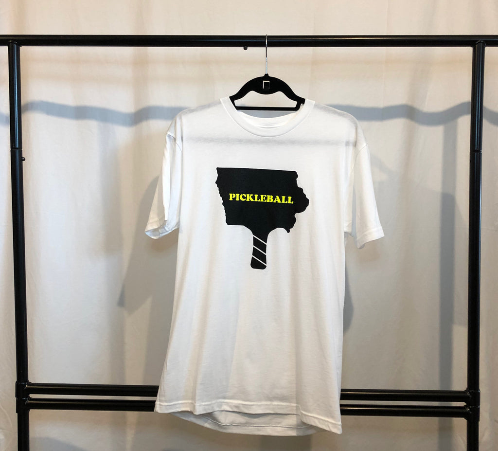 classic white t-shirt hanging from a hanger featuring the outline of iowa in black in the shape of a pickleball paddle with "pickleball" in the state outline in neon yellow