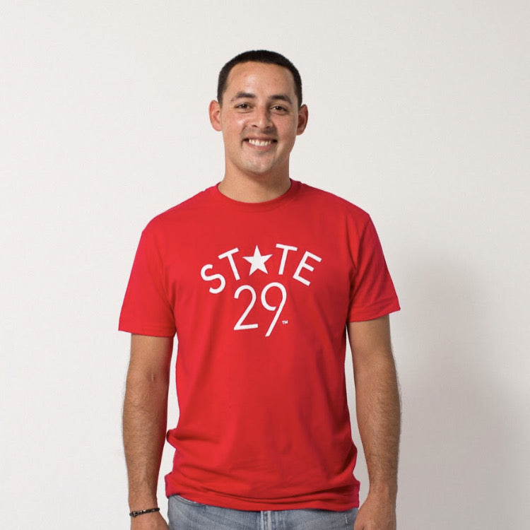 young male wearing a red tee with the 29th state apparel logo in white on the front