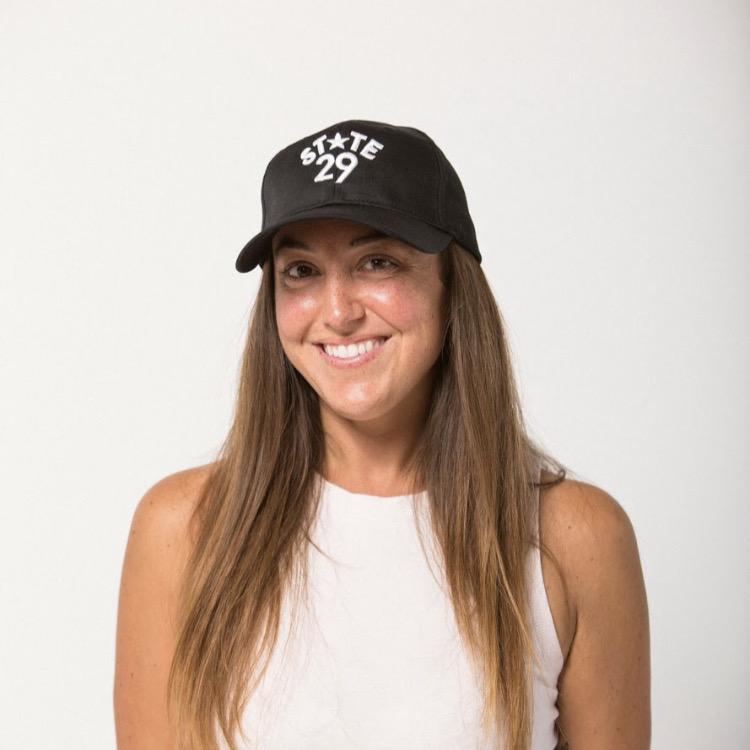 long dark haired young lady smiling wearing a 29th state apparel logo embroidered baseball hat