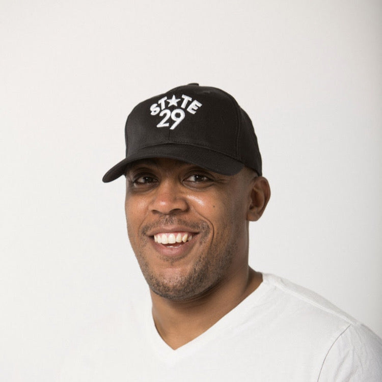 young man smiling in a white tee wearing a 29th state apparel logo baseball hat